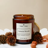 Candle jar labeled 'Autumn Woods' by Luca + Grey on a white surface with pinecones and nuts.
