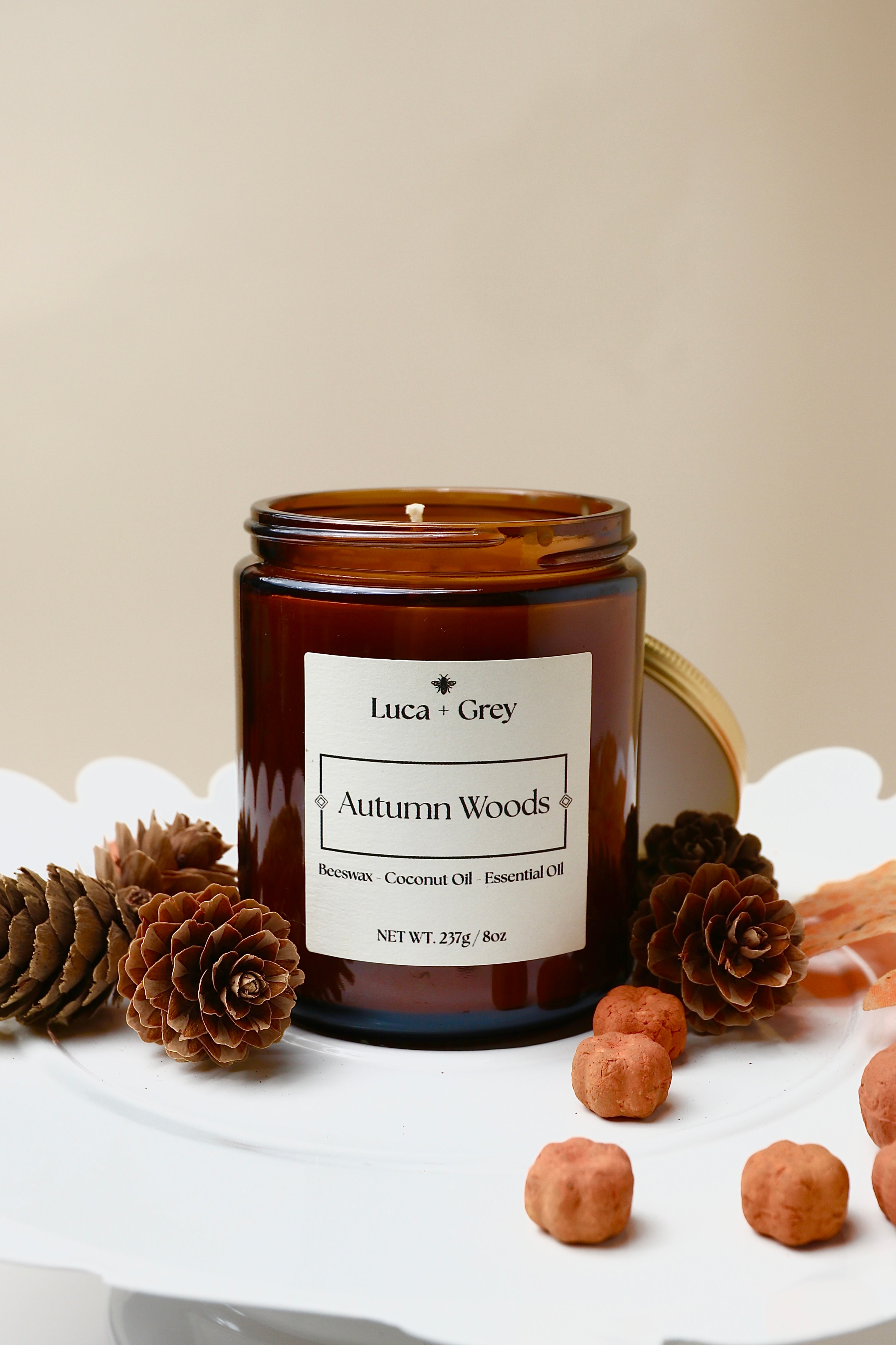Candle jar labeled 'Autumn Woods' by Luca + Grey on a white surface with pinecones and nuts.