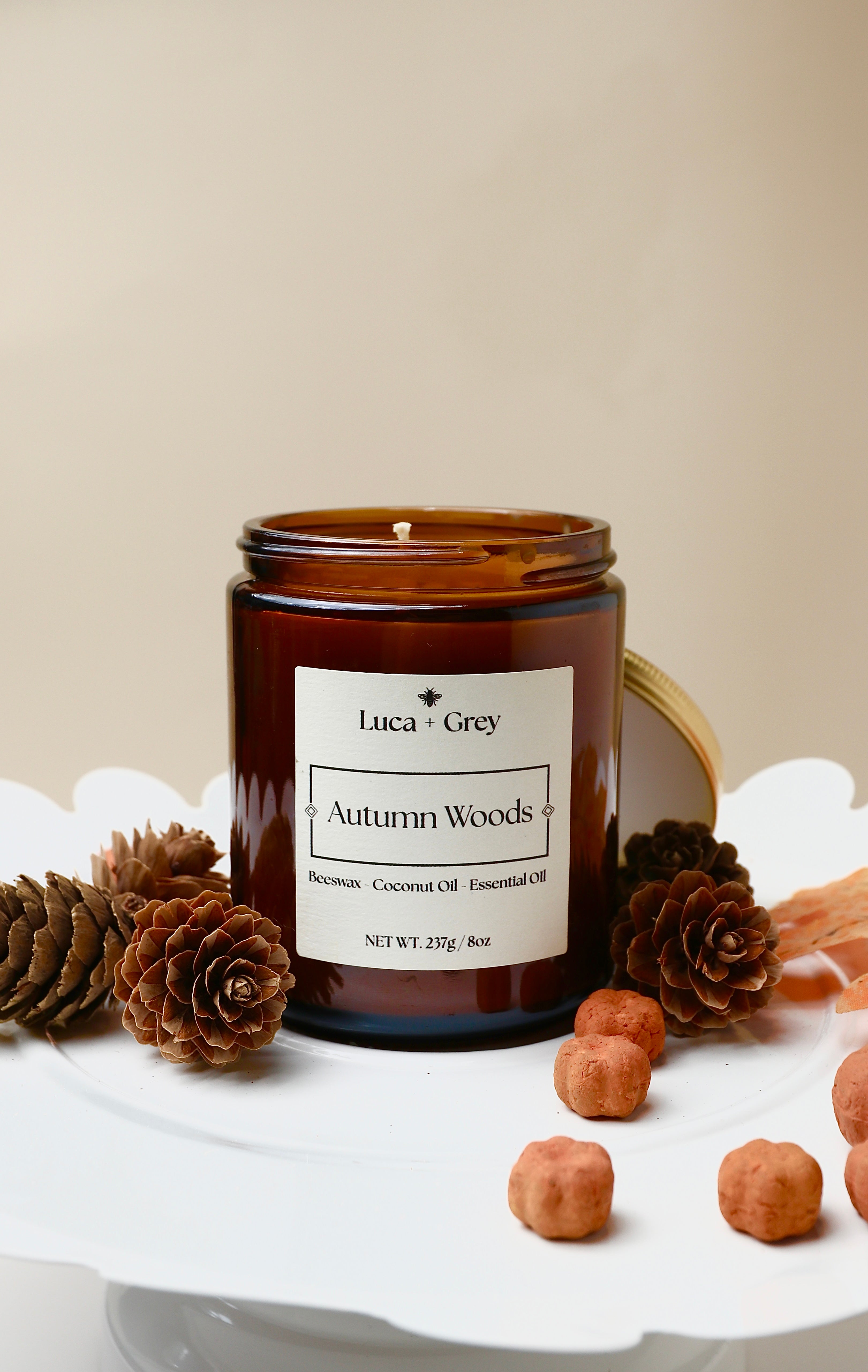 Candle jar labeled 'Autumn Woods' by Luca + Grey on a white surface with pinecones and nuts.