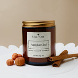Candle jar labeled 'Pumpkin Chai' by Luca + Grey on a white surface with cinnamon sticks and nuts.