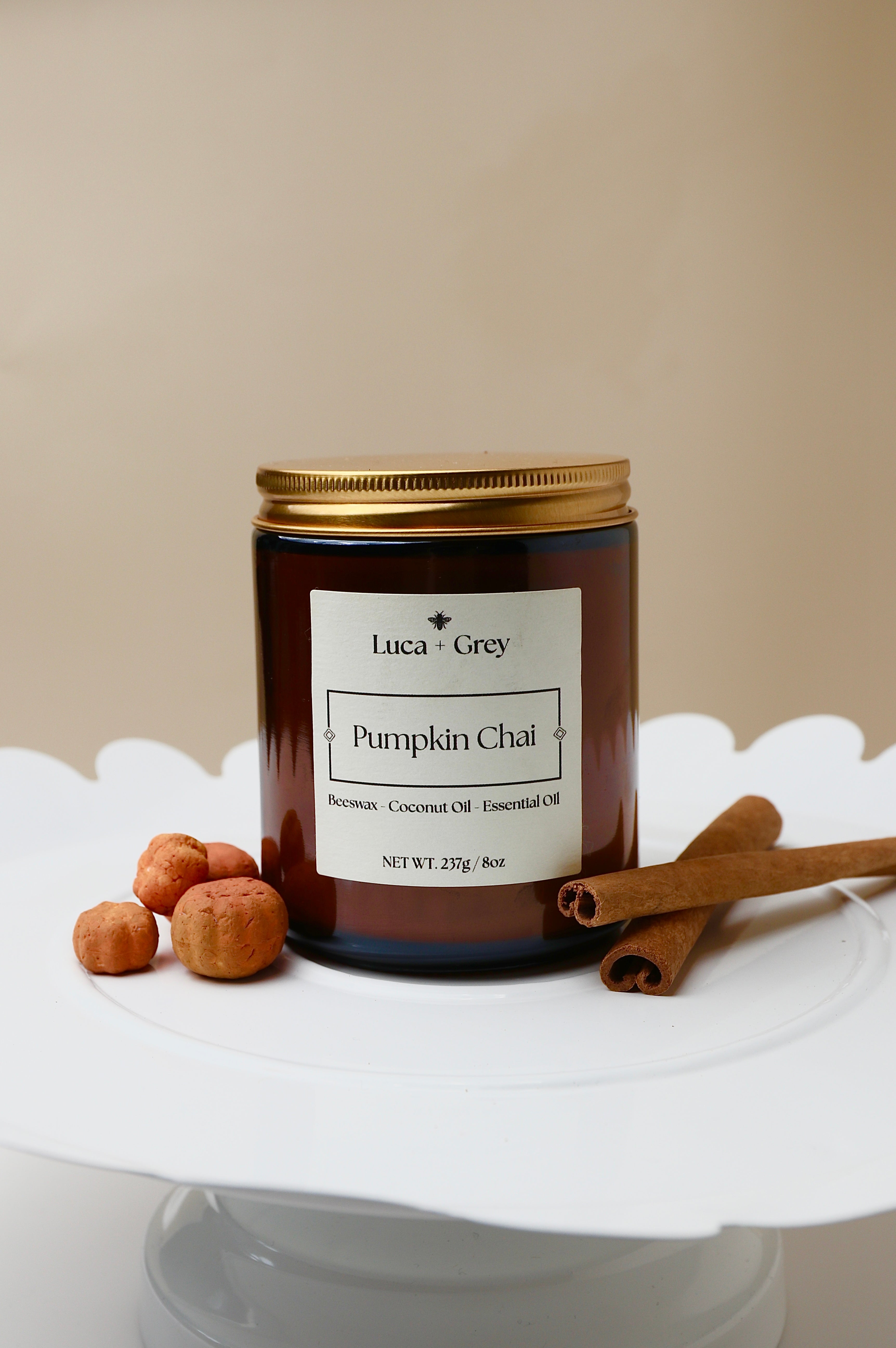 Candle jar labeled 'Pumpkin Chai' by Luca + Grey on a white surface with cinnamon sticks and nuts.