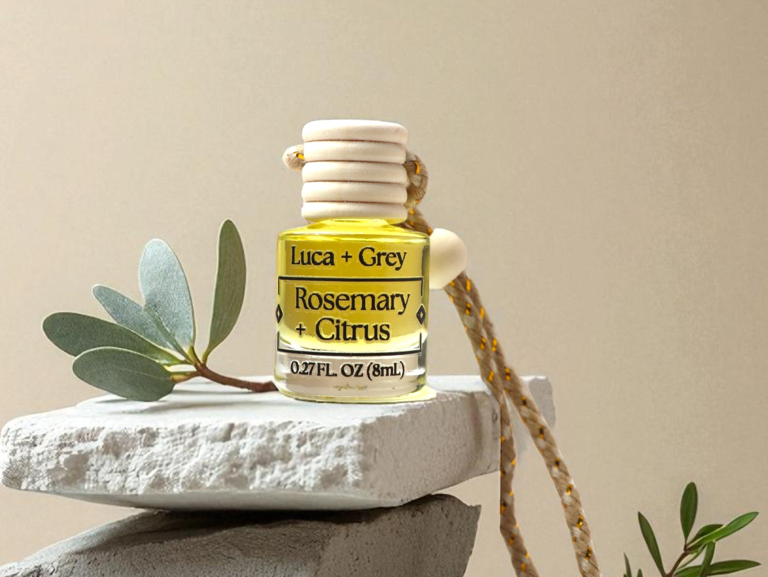 Small bottle of Luca & Grey Rosemary + Citrus essential oil on a stone surface with a beige background